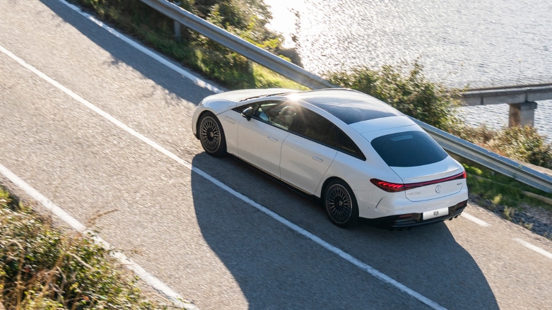 Auto eléctrico de lujo Mercedes-Benz EQS blanco manejando por carretera sobre la costa.